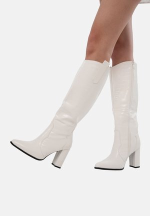 Botas blancas hasta la rodilla con un acabado brillante en charol, textura de cocodrilo, puntera puntiaguda y tacón transparente grueso. Incluye detalle de cremallera lateral.
