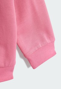 Lång rosa sweatshirtärm med ribbad struktur och elastiska ärmmuddar. Slät tyg med subtil lyster, designad för komfort och värme.