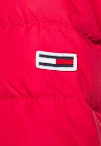 Tissu rembourré rouge avec une petite pièce rectangulaire cousue dessus, présentant des rayures horizontales noires, blanches et rouges.