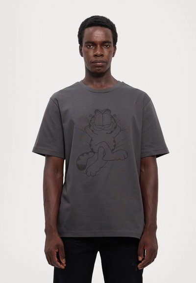 T-shirt en coton gris à manches courtes avec un dessin en ligne noire d'un chat cartoon allongé sur le devant. Col rond.