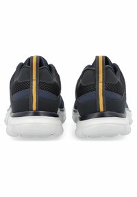 Zapatillas deportivas negras con parte superior de malla, cuello acolchado, franja de acento amarilla y suela de goma blanca. Vista trasera que destaca los detalles de diseño.