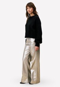 Zwarte, pluizige cropped trui gecombineerd met metallic zilveren wijde broekspijpen, met een gladde textuur en strakke lijnen. Eenvoudig zwart schoeisel.