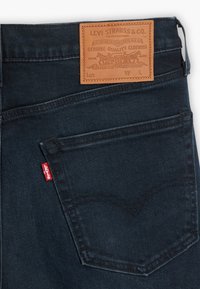 Ciemne dżinsy z denimu z naszywką ze skóry z wytłoczonym logo, klasycznym projektem tylnych kieszeni oraz czerwonym detalem z boku.