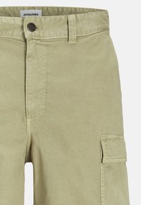Shorts cargo en coton vert clair avec fermeture à boutons, coutures visibles et poches latérales. Le tissu a une texture lisse.