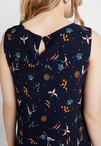 Mörkblå ärmlös klänning med en blomsterdesign i livfulla färger, med ett nyckelhål i ryggen och en texturerad tyg.