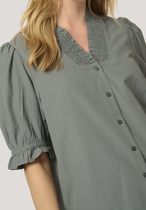 Jasnoszara bluzka z marszczonym dekoltem, bufkami na krótkich rękawach i zapięciem na guziki z przodu. Miękka tkanina o subtelnej teksturze.