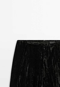 Jupe en velours noir avec une fermeture éclair latérale et une bande à la taille, présentée sur fond blanc, mettant en valeur la texture et les détails du tissu.