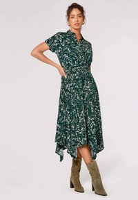 Korte mouw, groene jurk met een bladerenpatroon, met een ceintuur in de taille en een hoge-lage zoom. Persoonlijk gecombineerd met olijfgroene enkellaarsjes.