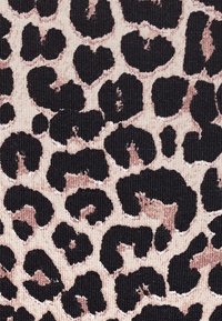 Taches de léopard irrégulières noires et brunes sur un tissu tricoté beige clair en arrière-plan.