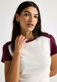 Vit t-shirt med vinröda korta ärmar, gjord av slät tyg. Har en rund halsringning och en smal passform, med en minimal design utan synliga mönster.