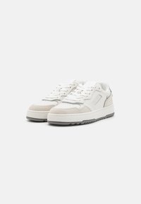 Sneakers bianchi con tomaia in pelle liscia, dettagli in camoscio e suola in gomma texturizzata. Caratterizzati da lacci piatti e un design semplice.