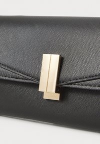 Svart texturerad kuvertväska med ett guld geometriskt spänne. Har en elegant design med en mjuk yta och subtilt mönster.