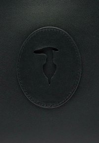 Czarna skórzana powierzchnia z okrągłym wytłoczonym wzorem wycięcia. Gładka tekstura i jednolity kolor z delikatnym przeszyciem wokół krawędzi.