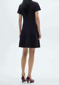 Robe à manches courtes, longueur au genou, en laine bleu marine foncé. Corsage ajusté avec texture côtelée, jupe évasée, associée à des chaussures à talons hauts couleur bordeaux.