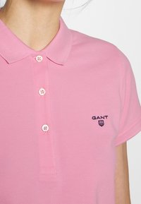 Polo shirt rosa realizzato in tessuto testurizzato con maniche corte, dotato di tre bottoni e un logo blu navy sul lato sinistro del petto.
