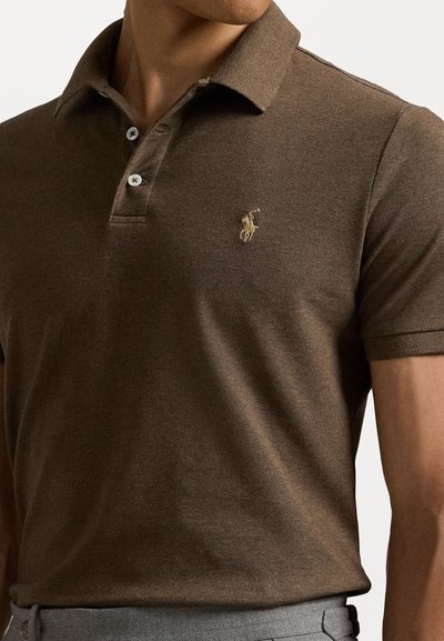 Polo brun avec un col classique, des manches courtes et une patte de boutonnage à trois boutons ; présentant un petit logo brodé en or sur la poitrine.