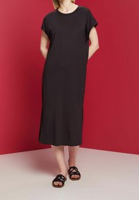 Robe noire, longueur midi, avec des manches courtes et un col rond. Confectionnée en tissu lisse avec des fentes sur les côtés. Associée à des sandales noires à talons.