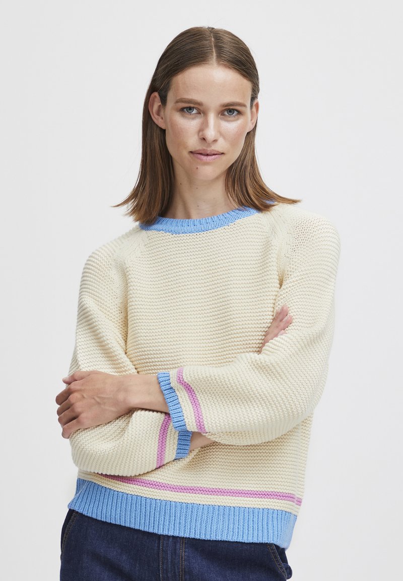 Strickpullover in Creme mit blauer Hals- und Ärmelbündchen, mit rosa und lila Streifen an den Ärmeln. Boxy-Schnitt, strukturierter Stoff.