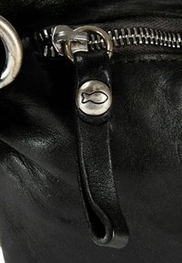 Tirador de cremallera de bolsa de cuero negro con un botón plateado que presenta un símbolo de pez grabado y dientes de cremallera de metal sobre cuero texturizado.
