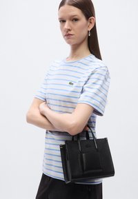Μαύρη υφασμάτινη τσάντα με δύο λαβές και μπροστινή τσέπη, συνοδευόμενη από γαλάζιο και λευκό ριγέ βαμβακερό t-shirt.