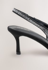 Čierne sandále na podpätku so zadným remienkom, zdobené tenkým remienkom s priehľadnými kamienkami, jemnou semišovou textúrou a štíhlym ihličkovým podpätkom.