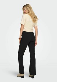 Top court à manches courtes crème associé à un pantalon noir évasé taille haute, complété par des bottines beiges. Texture de tissu lisse.