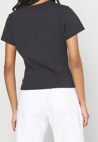 Svart t-shirt med kort ärm i bomull, med rund halsringning och en något beskuren design med logodetalj vid fållen.