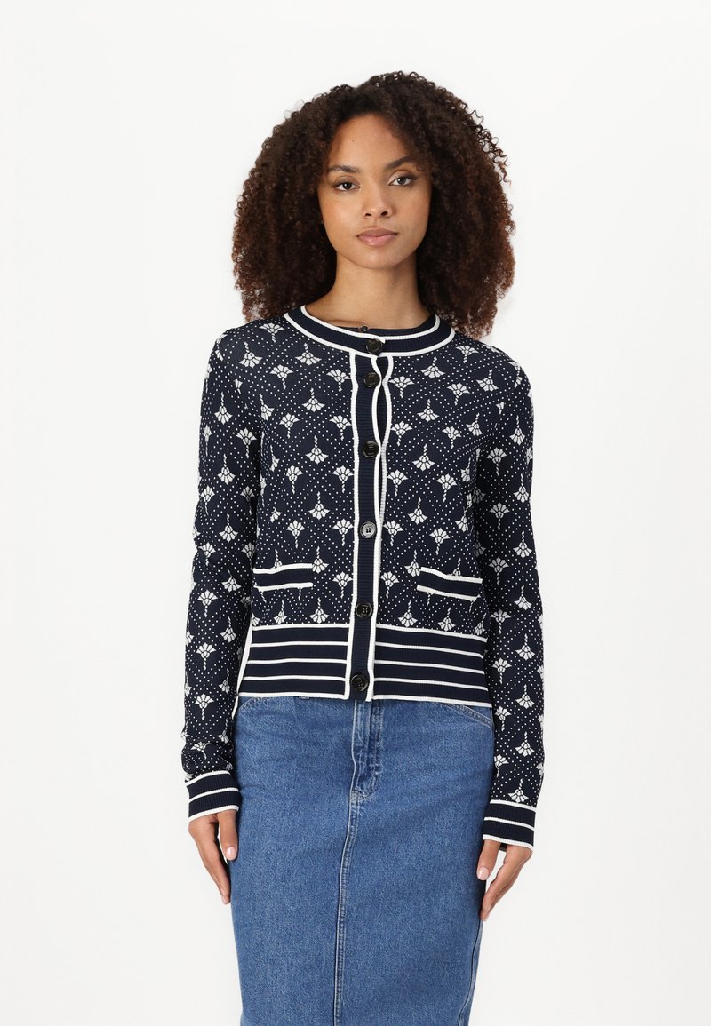 Navy cardigan with white floral pattern and details. Features a round collar, button closure, and two front pockets. Horizontal stripe accents.