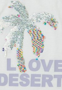 Tela blanca con un diseño de palmera adornada con brillantes lentejuelas plateadas y lentejuelas redondas de colores, acompañada del texto "ME ENCANTA EL DESIERTO" en lavanda.