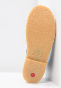 Semelle extérieure en caoutchouc marron avec une surface texturée, arborant un point rouge et le logo "Kickers" en relief. La chaussure est placée sur un fond blanc.
