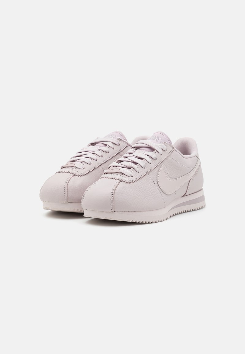 Zapatillas Nike en suave piel rosa, con puntera redondeada, cierre de cordones en la parte delantera y parte superior texturizada con el diseño característico del swoosh. Suela clásica.