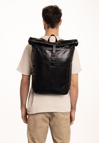 Sac à dos rouleau noir en cuir lisse. Il dispose de sangles réglables et d'une fermeture à boucle. Design minimaliste avec une silhouette épurée.