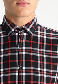 Svart rutigt skjorta med röda och vita rutor, en knapp-ner krage och svarta knappar, tillverkad av ett strukturerat tyg.