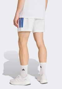 Witte atletische shorts met blauw en rood verticale strepen, gecombineerd met witte sokken en schoenen, voorzien van gladde stof en strakke lijnen.