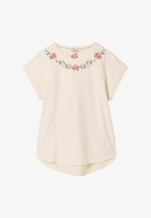 Kremowy top z krótkim rękawem z kwiatowym haftem w kolorach różu, niebieskiego i zielonego przy dekolcie; casualowy, luźny krój i zaokrąglony dół.