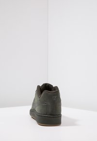 Zelené semišové tenisky s nízkým střihem, texturovanými akcenty a gumovou podrážkou. Logo viditelné na patě a na boku v tmavší zelené.