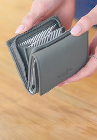 Pilkas odinis piniginė su užtrauktuku, viduje su dryžuotu pamušalu ir kortelių kišenėmis, laikoma rankoje prieš medinį paviršių.