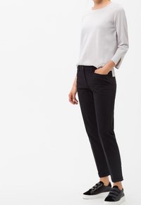 Světle šedé tričko s dlouhým rukávem, černé fitted kalhoty a černé tenisky s přezkami; hladká látka, přizpůsobený střih a minimalistický design.