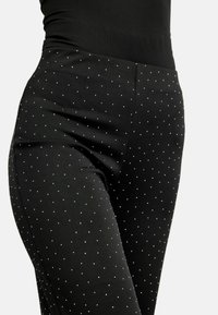 Mustad tihedalt istuvad püksid, millel on sile tekstuur, valged täpikesed ja laiali puistatud hõbedased aktsendid. Disainitud õhukeseks, kohandatud lõikeks.