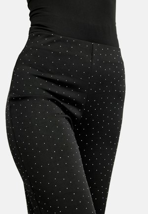 Sorte tætsiddende bukser med en glat tekstur, prydet med hvide polkaprikker og spredte sølvfarvede accenter. Designet til en elegant, skræddersyet pasform.