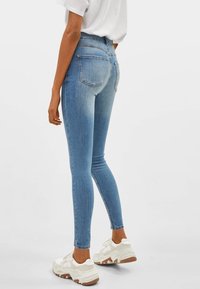 Höga blå denim skinny jeans med en slät textur, subtila blekningar och två bakfickor. Kommer med vita klumpiga sneakers.