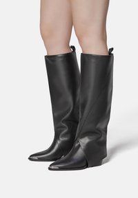 Black leather knee-high boots with a sleek design, pointed toe, and wedge heel; features a fold-over top and smooth texture.