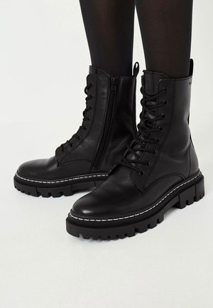 Stivali militari in pelle nera con finitura opaca, design con lacci, cerniera laterale e suola in gomma robusta con dettaglio di cucitura bianca.