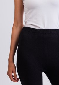 Zwarte, aansluitende legging met een geribde tailleband, gemaakt van een zachte, gestructureerde stof. Gekocht met een eenvoudige witte tanktop.