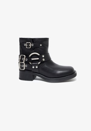Černá kožená kotníková bota s kulatou špičkou a nízkým blokovým podpatkem, s více stříbrnými přezkami a oválným kovovým akcentovým popruhem.