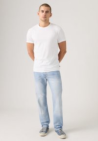 Balti medvilninė marškinėliai trumpomis rankovėmis, derinami su šviesiai mėlynais džinsais. Sportbačiai turi tamsiai mėlyną drobinį viršų ir baltą guminę pado dalį.