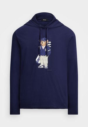 Sudadera con capucha de manga larga en color navy con un gráfico de un oso vestido con ropa deportiva, incluyendo un gorro, chaqueta y palos de golf. Elaborada en una tela suave con un ajuste clásico.