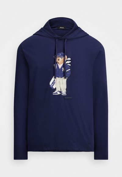 Tumesinine pikka varrukat hoodie, millel on karu graafika spordivariandis, kanda müts, jakk ja golfikepid. Valmistatud pehmest kangast, klassikaline lõige.