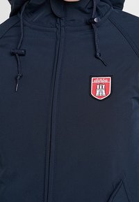 Marineblå hættejakke med høj krave, der har et rødt og hvidt broderet logo. Inkluderer justerbare snore og en glat tekstur.