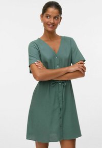 Abito a maniche corte con scollo a V in morbido tessuto verde. Presenta una chiusura con bottoni sul davanti e una vita con cordoncino per una vestibilità regolabile.